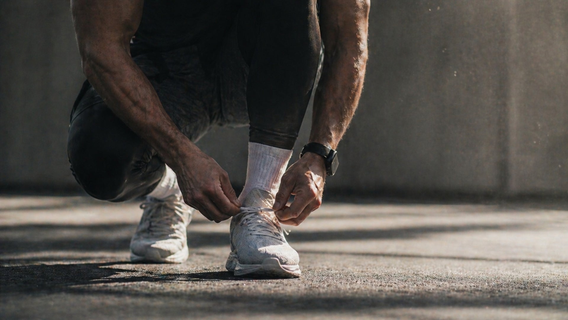 Person tying shoelaces on white sneakers in an urban setting